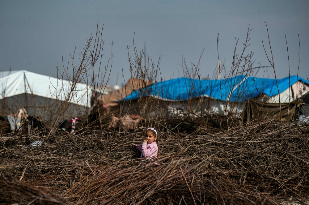 A displaced Syrian child stands in a pile of wood twigs used for cooking, at the Al-Younani camp on the outskirts of the northern city of Raqa. — AFP pic