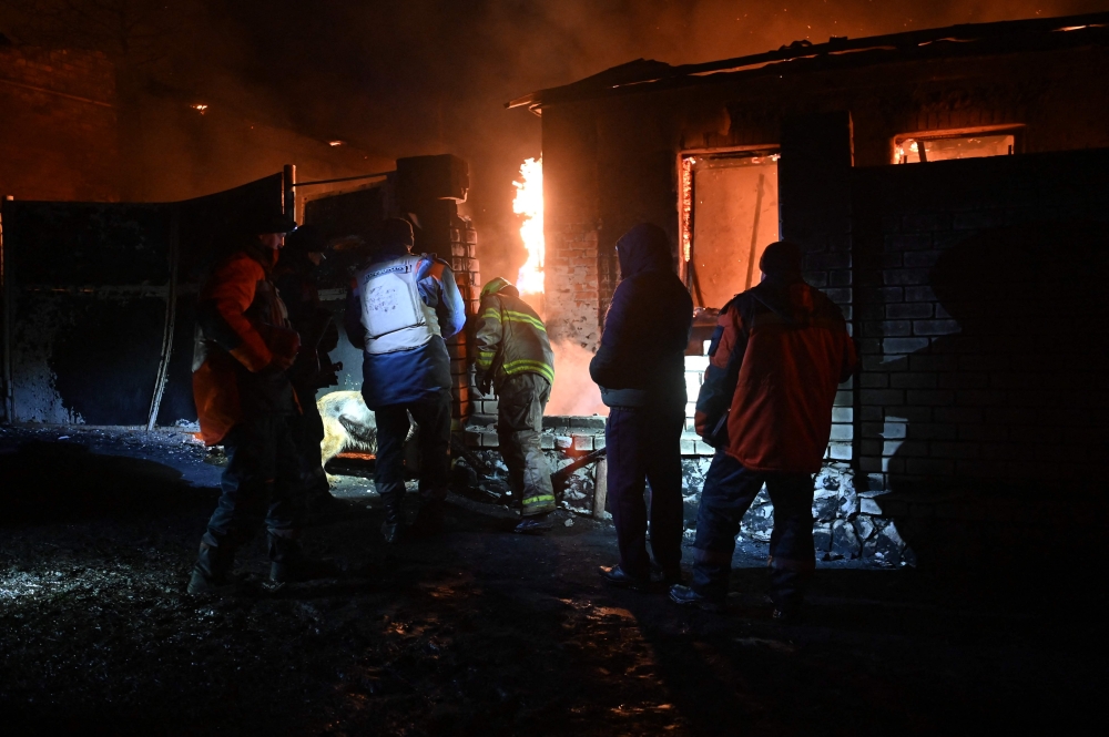 Ukrainian emergency and rescue personnel walk past a burning structure as they work at the site of a drone attack in Kharkiv, early on February 10, 2024. — AFP pic