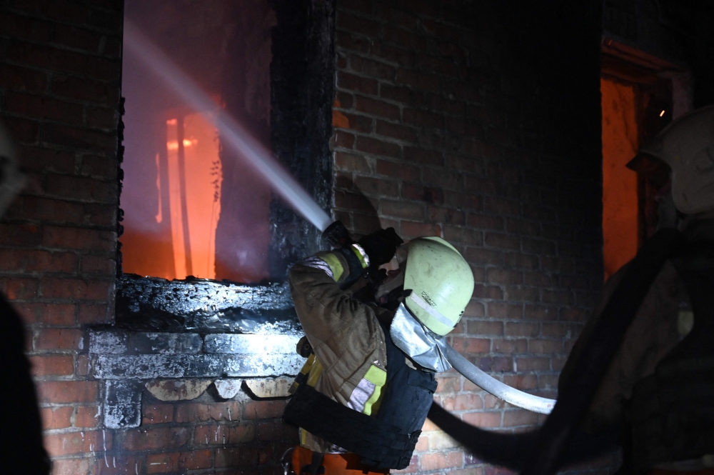 Ukrainian emergency and rescue personnel douse water to extinguish flames as they work at the site of a drone attack in Kharkiv, early on February 10, 2024. — AFP pic