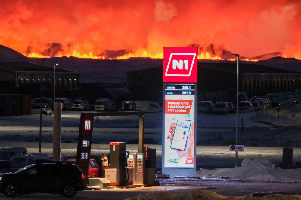 People filling up their vehicles at a petrol station as lava and billowing smoke pours out of a fissure during a volcanic eruption near Grindavik, western Iceland on February 8, 2023. — AFP pic