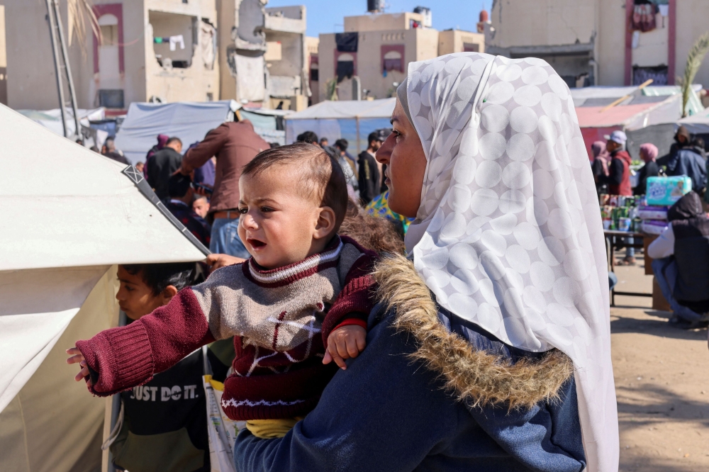 A displaced Palestinian woman holds her son as she waits to get him examined by a doctor, outside a medical tent, amid the ongoing conflict between Israel and Hamas, in Rafah in the southern Gaza Strip February 11, 2024. — Reuters pic