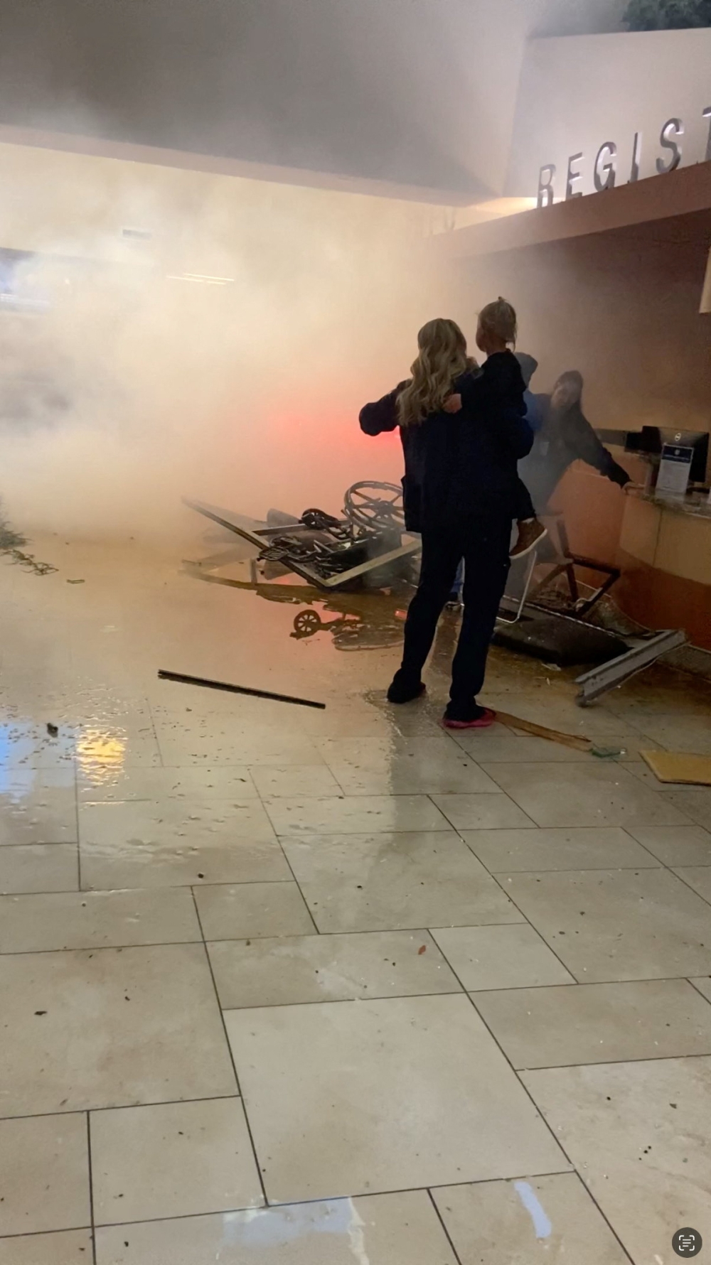 A woman holding a child stands near smoke rising from the site where a vehicle drove into the emergency room at St. David's North Austin Medical Center in Austin, Texas, February 13, 2024, in this screengrab obtained from a social media video. — Stephen Hughes/via Reuters pic