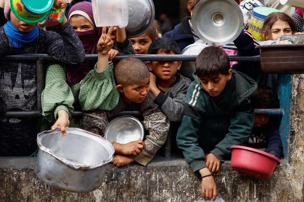 Palestinian children wait to receive food from a charity kitchen in Rafah. — Reuters pic
