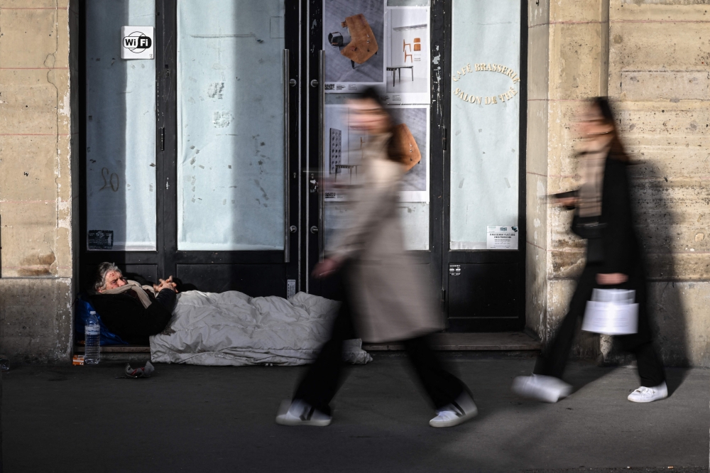 File photo of pedestrians walking past a homeless person lying on the sidewalk in centre Paris on February 15, 2024. ― AFP pic