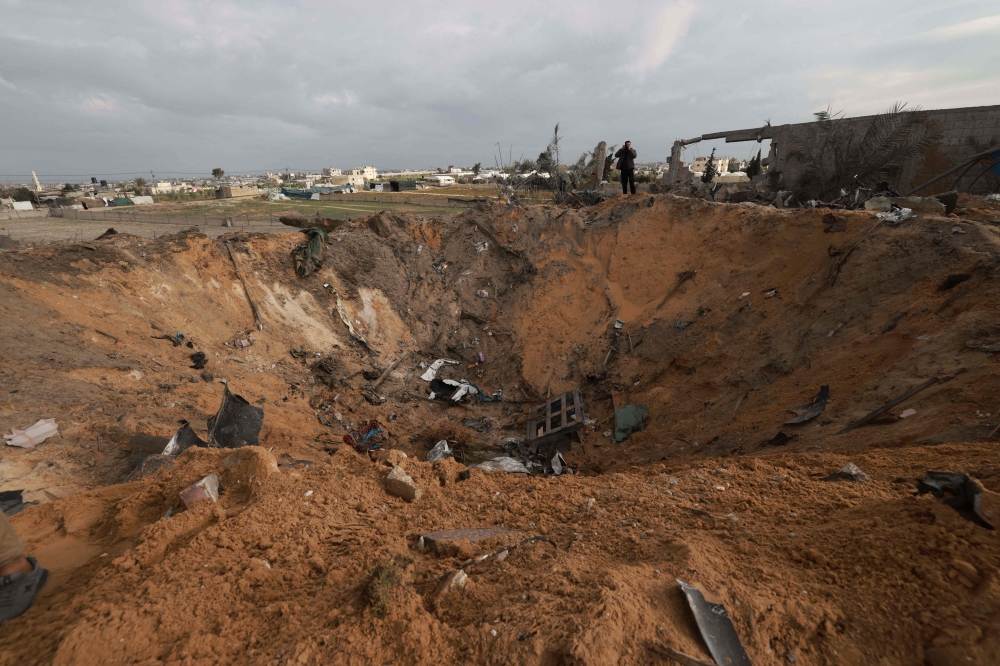 A Palestinian stands next to a huge crater in Rafah on February 18, 2024, following Israeli air strikes on the southern Gaza Strip border city amid ongoing battles between Israel and the Palestinian Hamas movement. — AFP pic