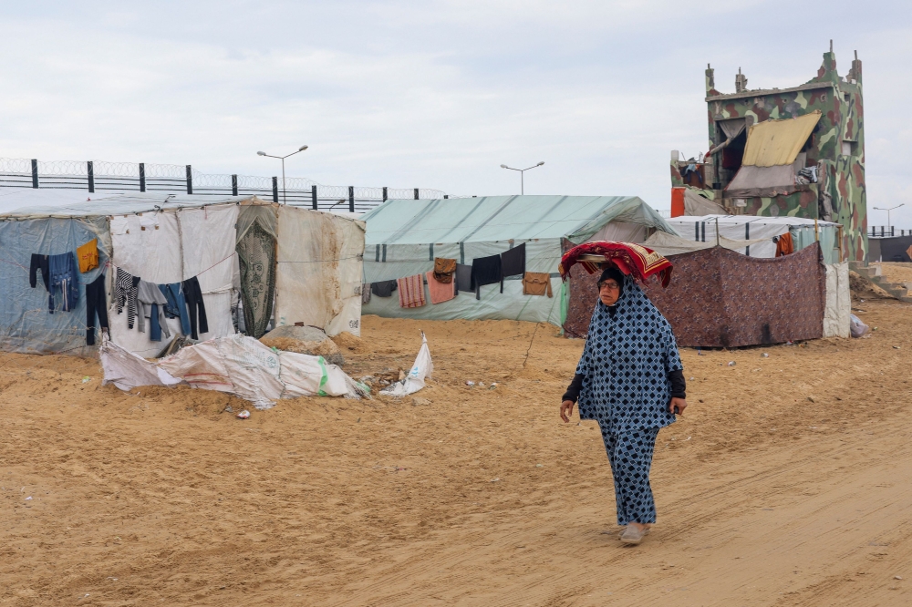 A displaced Palestinian woman, who fled her house due to Israeli strikes, amid the ongoing conflict between Israel and the Palestinian Islamist group Hamas, carries a tray with bread on her head as she walks past the border with Egypt, amid fears of an Israeli ground assault in Rafah, in the southern Gaza Strip February 18, 2024. — Reuters pic