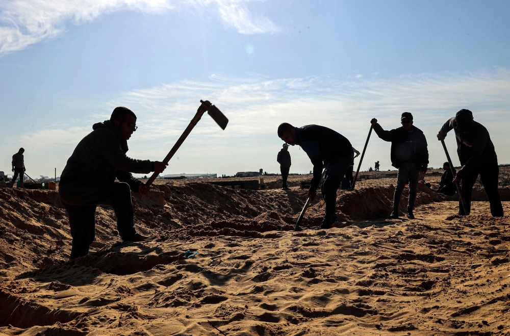 Men dig graves for Palestinians killed during overnight Israeli bombing at a cemetery in Rafah. — AFP pic