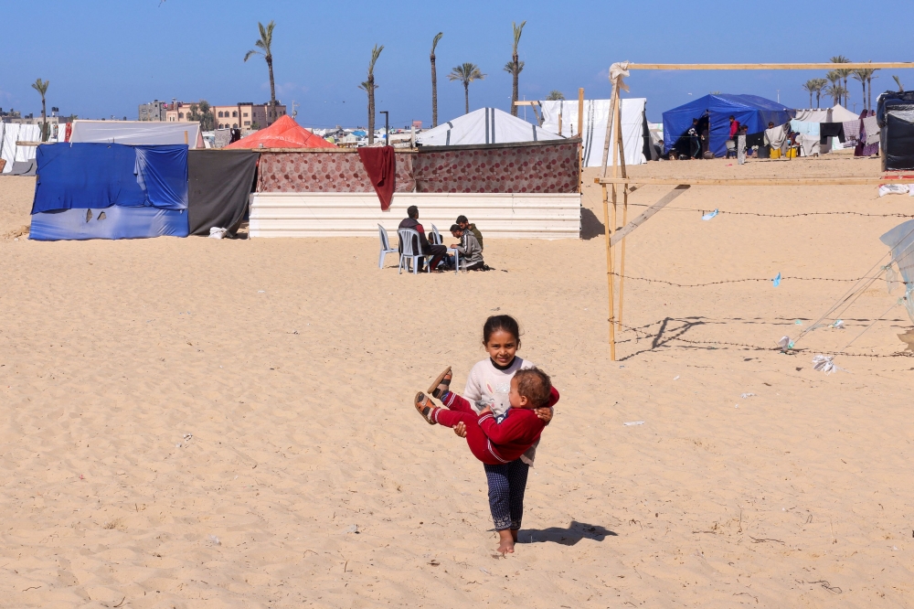 A displaced Palestinian girl holds her brother at a tent camp where they shelter, amid the ongoing conflict between Israel and Hamas, in Rafah in the southern Gaza Strip February 21, 2024. — AFP pic