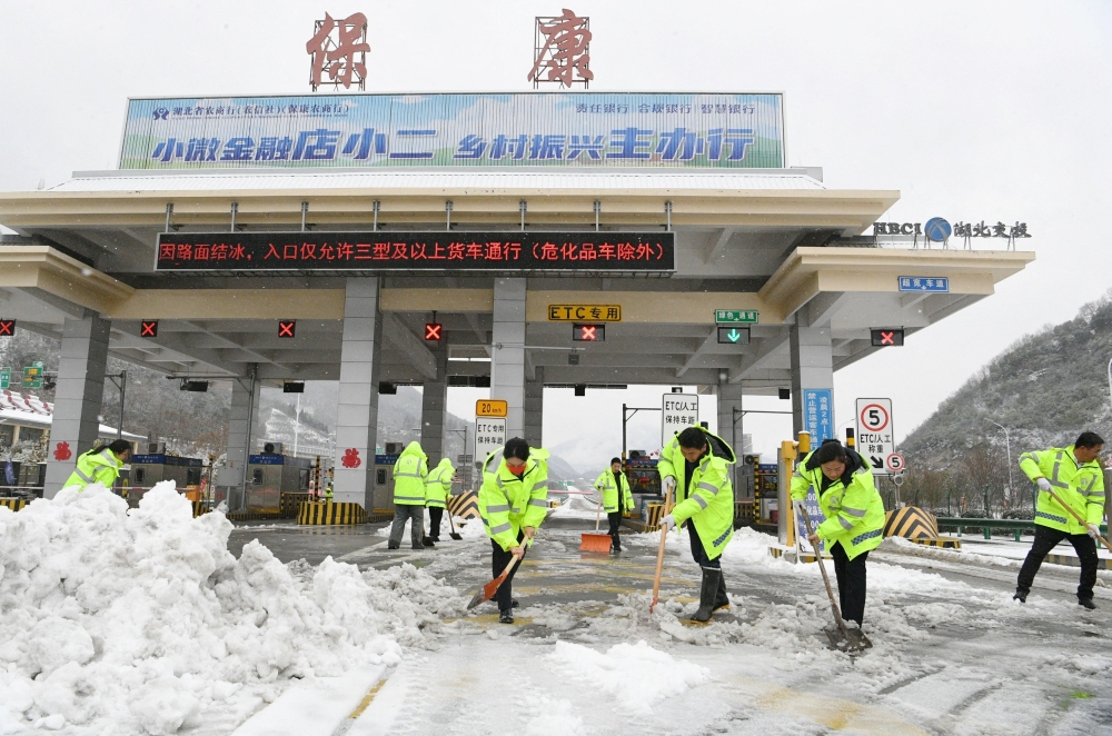 Workers remove snow from a highway toll station following snowfall in Baokang county of Xiangyang, Hubei province, China. — Reuters pic