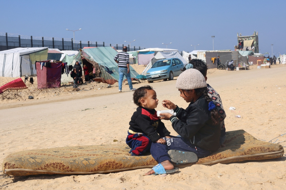 Displaced Palestinian girl, who fled her house due to Israeli strikes, feeds her brother at a tent camp, near the border with Egypt, in Rafah in the southern Gaza Strip, February 25, 2024. — Reuters pic
