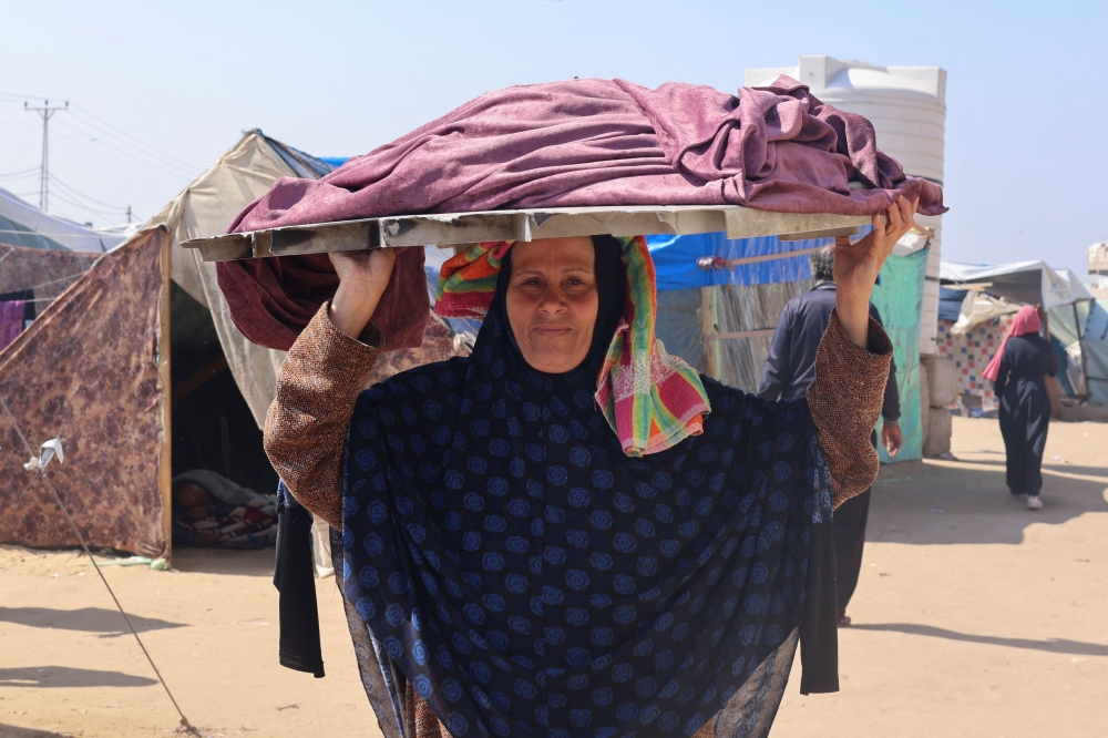 A displaced Palestinian woman, who fled her house due to Israeli strikes, carries a tray of bread on her head, at a tent camp in Rafah, in the southern Gaza Strip February 25, 2024. — Reuters pic