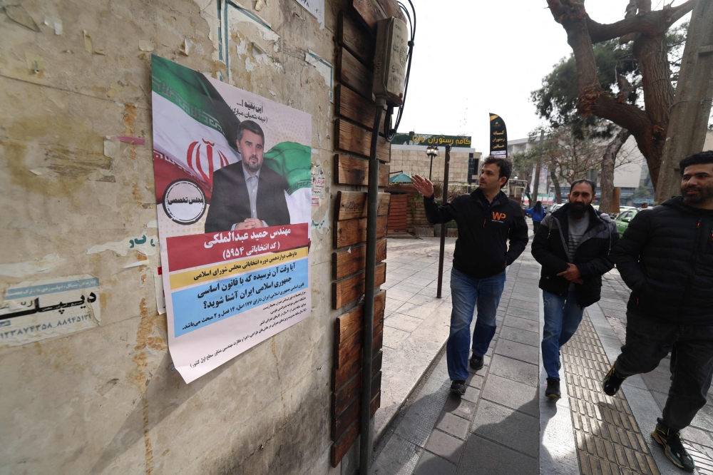 Men walk past a wall bearing an electoral campaign poster, ahead of the upcoming elections, in Tehran on February 24, 2024. Voters are due to cast their ballots on March 1 to pick new members of Iran's parliament, as well as the Assembly of Experts, a key body in charge of appointing the country's supreme leader. — AFP pic