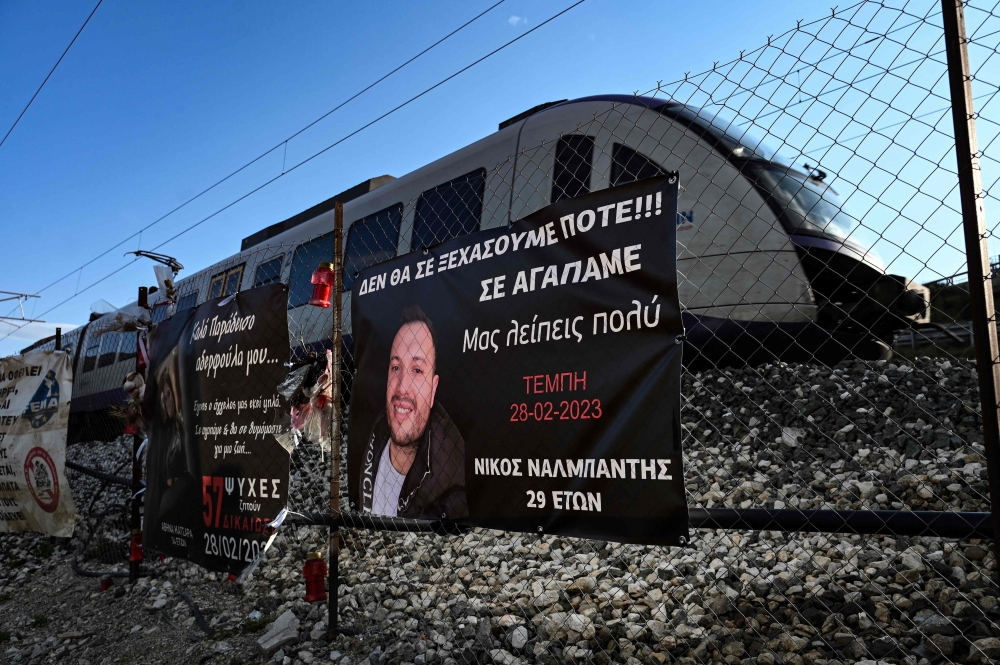 This picture taken on February 24, 2024, in the Valley of Tempi, near Larisa shows a Hellenic Train rolling past banners at the site where 57 people, mostly students, lost their lives in a train crash in 2023. — AFP pic