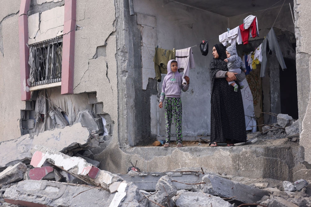 A Palestinian woman holds her child as she stands at a house damaged in Israeli strikes, as the conflict between Israel and Hamas continues, in Rafah in the southern Gaza Strip, February 27, 2024. — Reuters pic