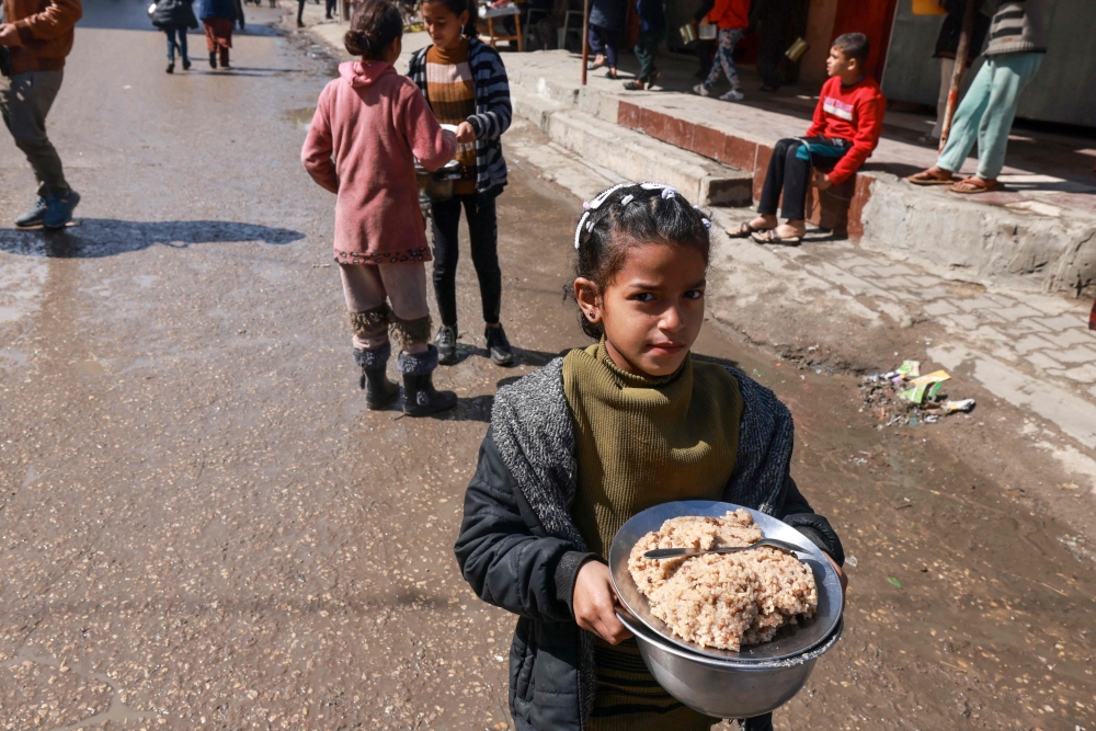 A displaced Palestinian child carries a plate of rice near a food distribution point in Rafah in the southern Gaza Strip on March 8, 2024, amid the ongoing conflict between Israel and Hamas militants. — AFP pic