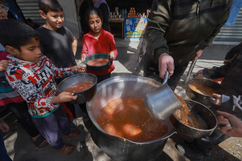 Palestinian children receive cooked food rations as part of a volunteer youth initiative in Rafah. — AFP pic