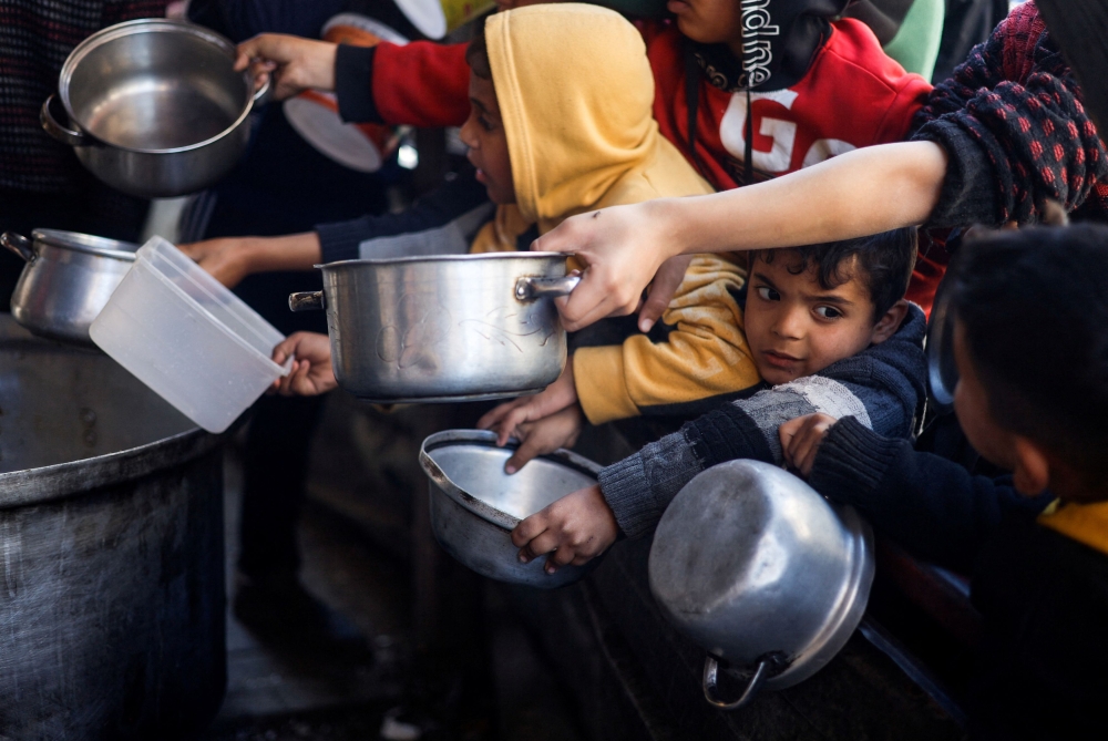 Palestinian children wait to receive food cooked by a charity kitchen amid shortages of food supplies. — Reuters pic