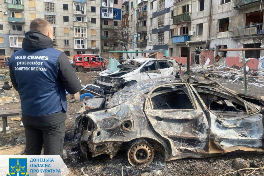 This handout photograph taken and released  by Donetsk Region Prosecutor`s Office on March 10, 2024 shows a war crimes prosecutor standing next to destroyed cars in the courtyard of a damaged residential building following a missile attack in Myrnohrad, Donetsk region. — Donetsk Region Prosecutor`s Office via AFP pic