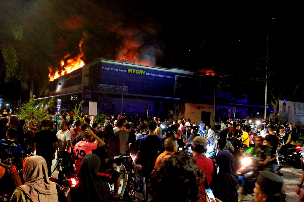 Onlookers watch as Fire and Rescue Department personnel attempt to put out the blaze at the Mydin Hypermarket in Manjoi, Ipoh, March 10, 2024. — Bernama pic