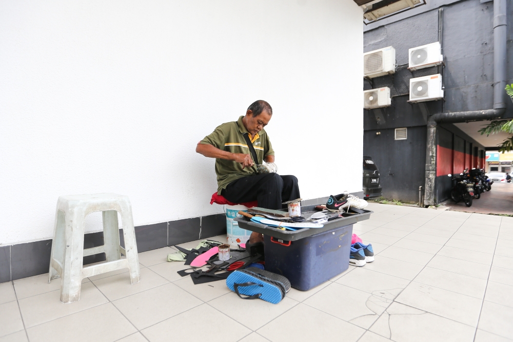 A shoemaker, Mahyudin, continues to work during the fasting month of Ramadan in Petaling Jaya, March 12, 2024. Although Mahyudin does not mend shoes directly under the sun, he is no stranger to the hot breeze along the streets and reflections of the scorching sun bouncing onto him by passing cars. — Picture by Miera Zulyana