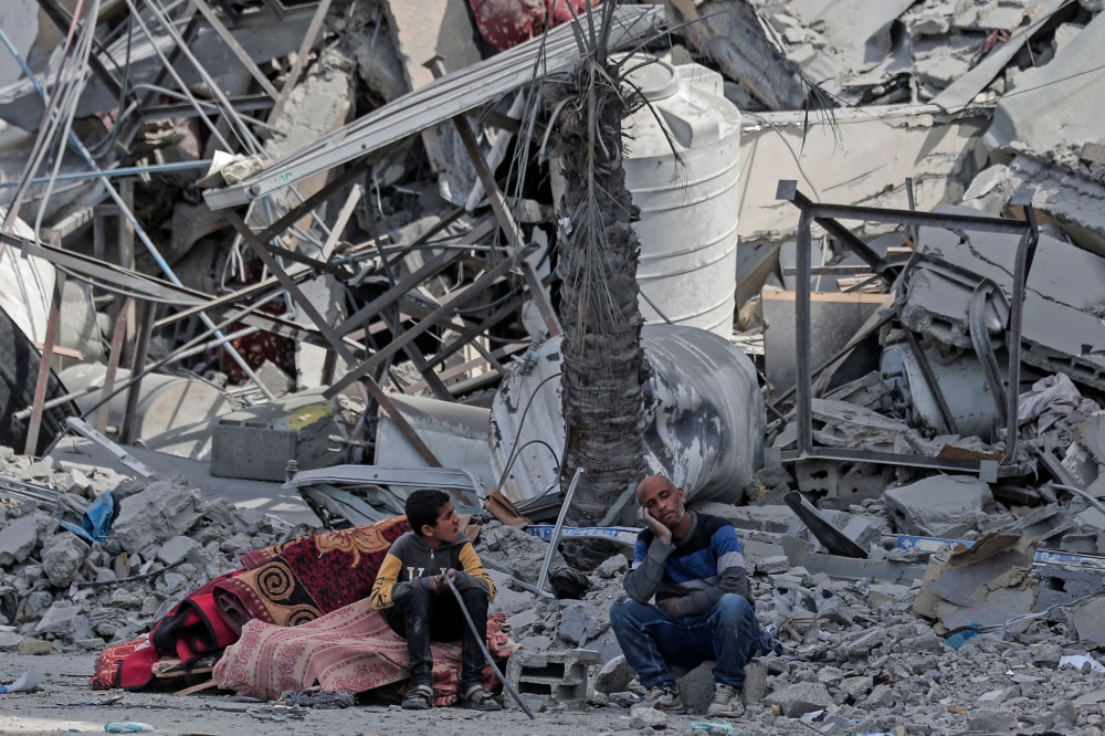 Displaced Palestinians sit with their belongings amid the rubble of houses destroyed by Israeli bombardment in Hamad area, west of Khan Yunis. — AFP pic