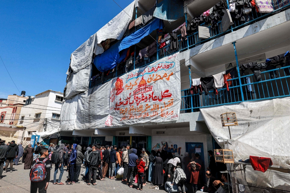 Palestinians gather to receive humanitarian aid at a camp sheltering displaced Palestinians erected in a school run by the United Nations Relief and Works Agency for Palestine Refugees (UNRWA) in Rafah in the southern Gaza Strip on March 13, 2024. — AFP pic