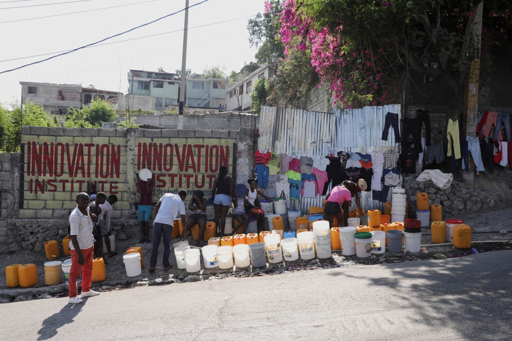 People line up along a street to collect water in buckets and containers in Port-au-Prince. — Reuters pic