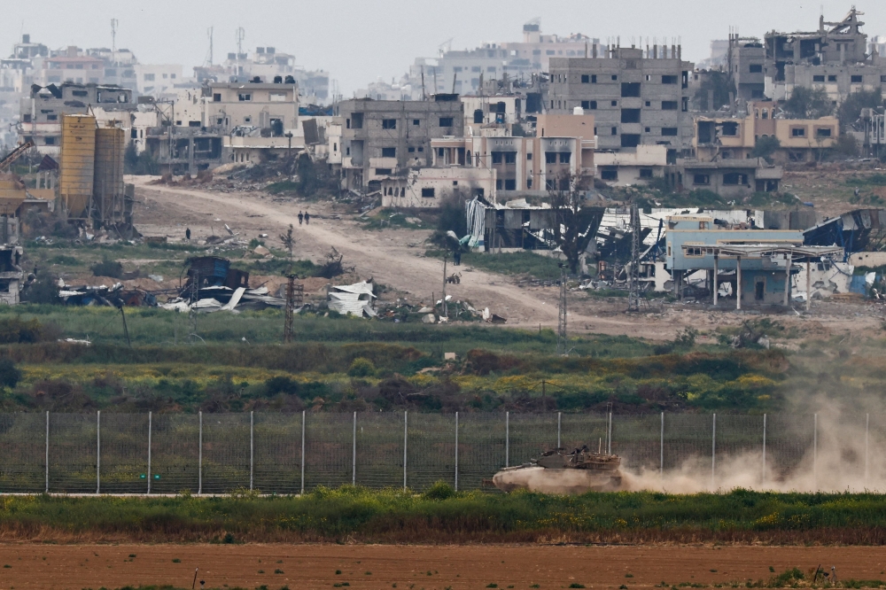 A tank maneuvers near the Israel-Gaza border on the Israeli side as people walk inside Gaza, amid the ongoing conflict between Israel and the Palestinian Islamist group Hamas, as seen from Israel, March 17, 2024. — Reuters pic