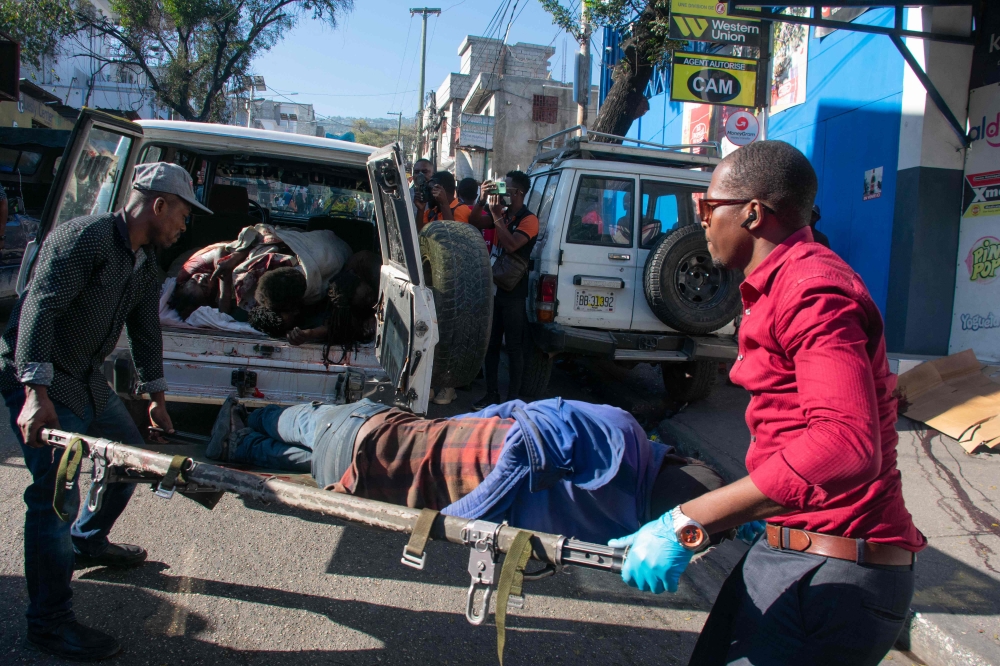 Paramedics carry the body of a person who was among a dozen killed in the street by gang members in an affluent suburb of Haiti’s capital. — AFP pic