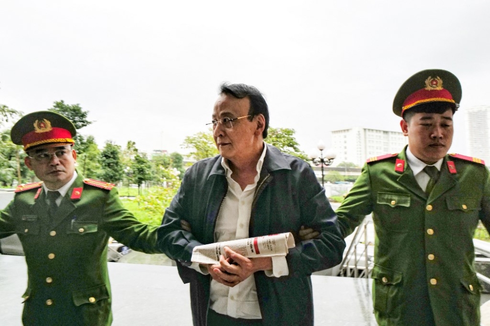 Chairman of Tan Hoang Minh group Do Anh Dung (centre) is escorted by police officers to a court for his trial on fraud charges in Hanoi on March 19, 2024 A top Vietnamese property tycoon went on trial on March 19, 2024 accused of cheating thousands of investors in a US$355 million bond scam, in the communist nation’s latest criminal case targeting high-flying business leaders. — AFP pic