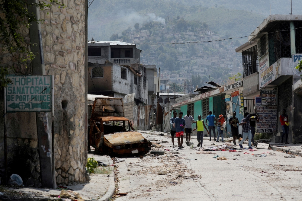 People walk past a damaged car in the Carrefour Feuilles neighbourhood, which was deserted due to gang violence. — Reuters pic