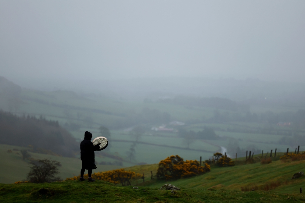 A reveller plays the bodhran drum to celebrate the arrival of Spring Equinox on top of Sliabh na Caillaigh at dawn to watch the sunrise during bad weather over the ancient Loughcrew megalithic cairns, in Oldcastle, Ireland, March 20, 2024. — Reuters pic  