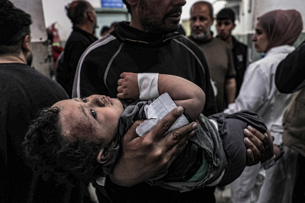 A man carries a child, injured in an Israeli air strike, to the trauma ward of Al-Najjar hospital in Rafah. — AFP pic
