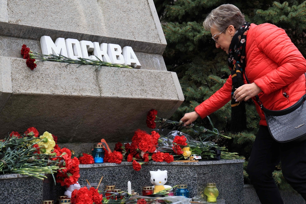 A woman lays flowers on a memorial stone reading 