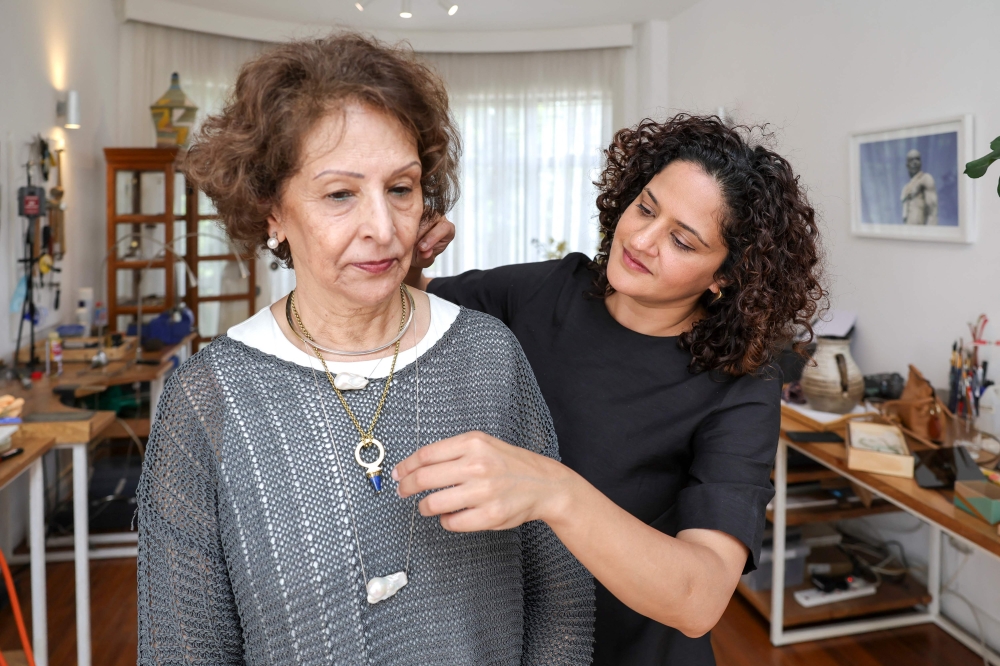 Kenyan designer Ami Doshi Shah (right) fits a client with one of her eclectic jewelry pieces at her home studio, where she creates eclectic hand-made jewelry crafted using locally sourced raw materials varying among semi-precious stones and metals, in Nairobi on February 16, 2024. — AFP pic