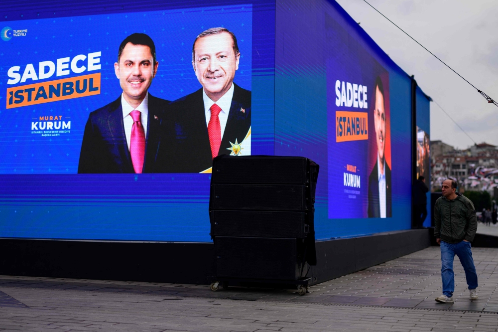 A man walks past an electoral poster displaying Justice and Development (AK) Party candidate Murat Kurum, with and with Turkey President Recep Tayyip Erdogan, in Istanbul on March 20, 2023, ahead of the local election of March 31. — AFP pic