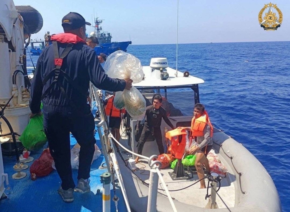 A member of Philippine Coast Guard personnel hands out supplies to the people onboard a rigid hull inflatable boat during a resupply mission in the South China Sea, March 23, 2024. — Armed Forces of the Philippines handout via Reuters