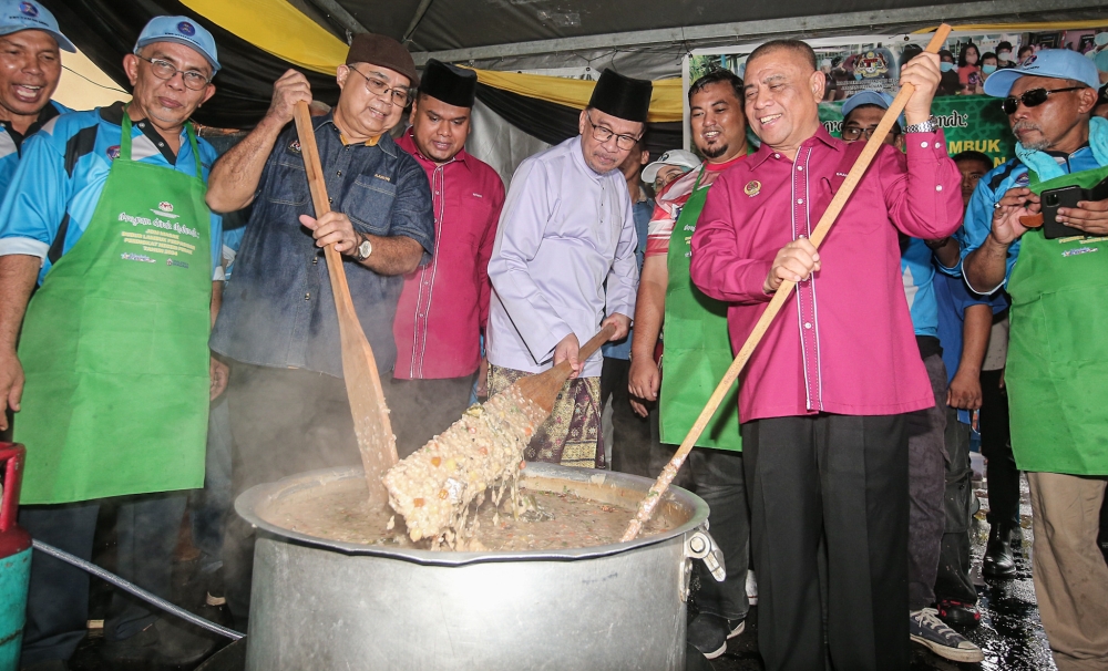 Prime Minister Datuk Seri Anwar Ibrahim stirs the bubur lambuk at the Madani Perdana programme at Dewan KRT Taman Meru, Perak, March 25, 2024. With him are Perak Menteri Besar Datuk Seri Saarani Mohamad and Unity Minister Datuk Aaron Ago Dagang. — Picture by Farhan Najib