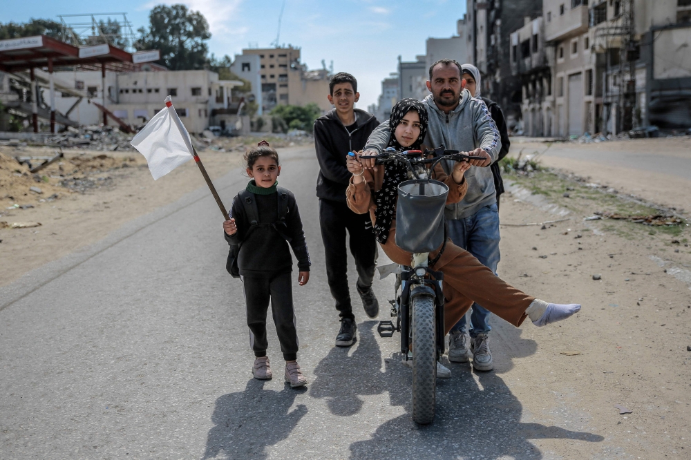 A girl holds a white flag as her displaced Palestinian family walks through Gaza City. — AFP pic