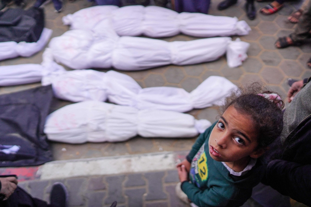 A Palestinian girl stands over shrouded bodies, killed in overnight Israeli bombardment, at Al-Aqsa Martyrs Hospital in Deir al-Balah on March 25, 2024. — AFP pic