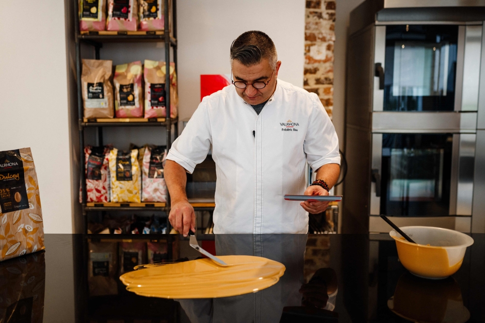 French pastry chef and creative director of Valrhona chocolaterie Frederic Bau prepares a 'blond' chocolate, oven-roasted apples and a Tahitian vanilla cream at Valrhona chocolatier in Paris on March 1, 2024. — AFP pic