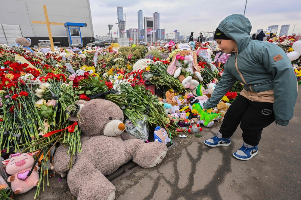 A child lays flowers at a makeshift memorial in front of the Crocus City Hall in Moscow's northern suburb of Krasnogorsk on March 29, 2024, a week after a deadly attack by gunmen on a Moscow concert hall, setting the building alight and killing at least 143 people. — AFP pic