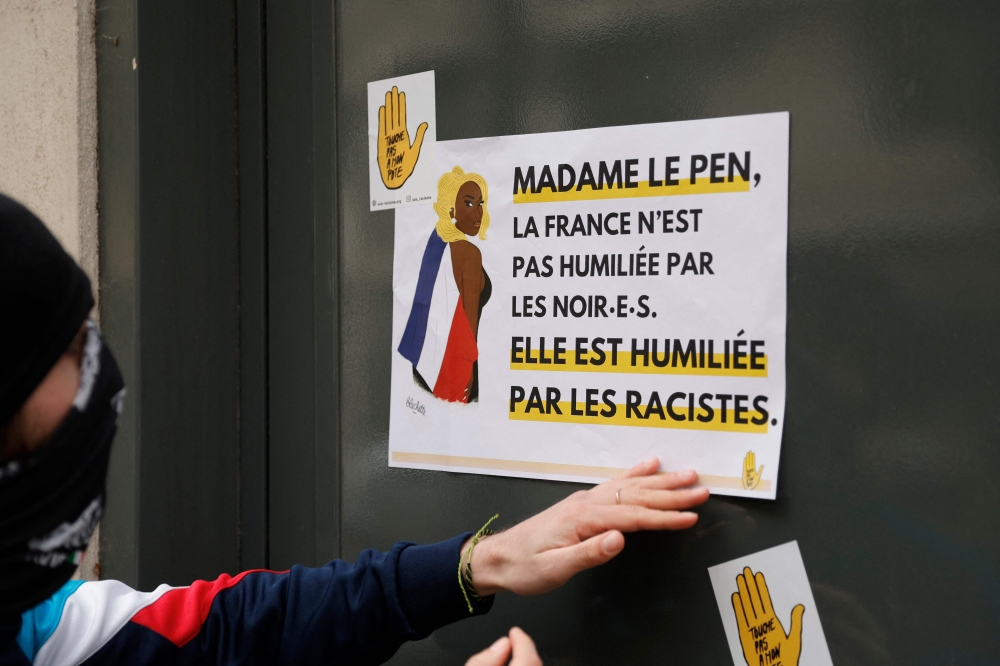 A demonstrator puts a sticker reading ‘Madame Le Pen, France is not being humiliated by blacks, it is being humiliated by racists’ on the Rassemblement National (RN) headquarters building during a rally organised by the French association SOS Racisme in Paris on March 24, 2024, in support of Aya Nakamura, following the numerous racist attacks on the French-Malian singer, who was mentioned as a possible participant in the opening ceremony of the 2024 Paris Olympic Games. — AFP pic