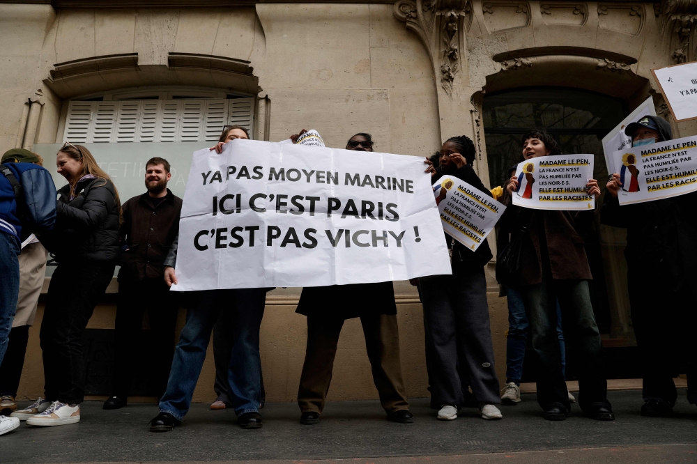 Demonstrators pose with a banner (centre) reading ‘there’s no way Marine, this is Paris not Vichy’ during a rally in front of the Rassemblement National (RN) organised by the French association SOS Racisme in Paris on March 24, 2024, in support of Aya Nakamura, following the numerous racist attacks on the French-Malian singer, who was mentioned as a possible participant in the opening ceremony of the 2024 Paris Olympic Games. — AFP pic 