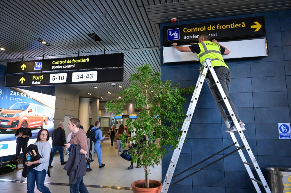 A Romanian worker changes the signs to lead passengers of the non-Schengen flights toward newly installed border control points inside the Henri Coanda International Airport in Otopeni, Romania March 28, 2024. — AFP pic