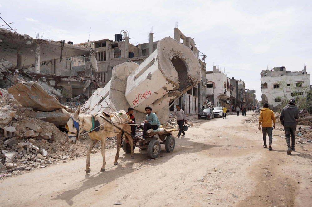 Palestinians walk past damaged and destroyed buildings in the Maghazi camp for Palestinian refugees in the central Gaza Strip on March 29, 2024, amid the ongoing conflict in Gaza between Israel and the Palestinian group Hamas. — AFP pic