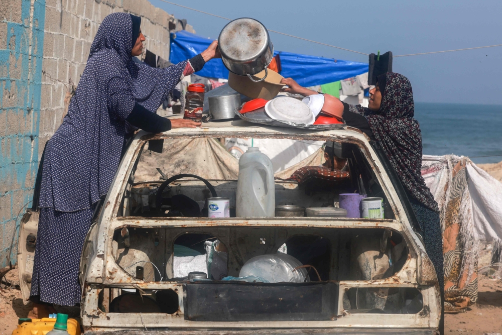 Palestinian women arrange kitchen utensils to dry atop a destroyed car at a makeshift camp for displaced people in Rafah in the southern Gaza Strip on March 30, 2024, amid the ongoing conflict between Israel and the militant group Hamas. — AFP pic