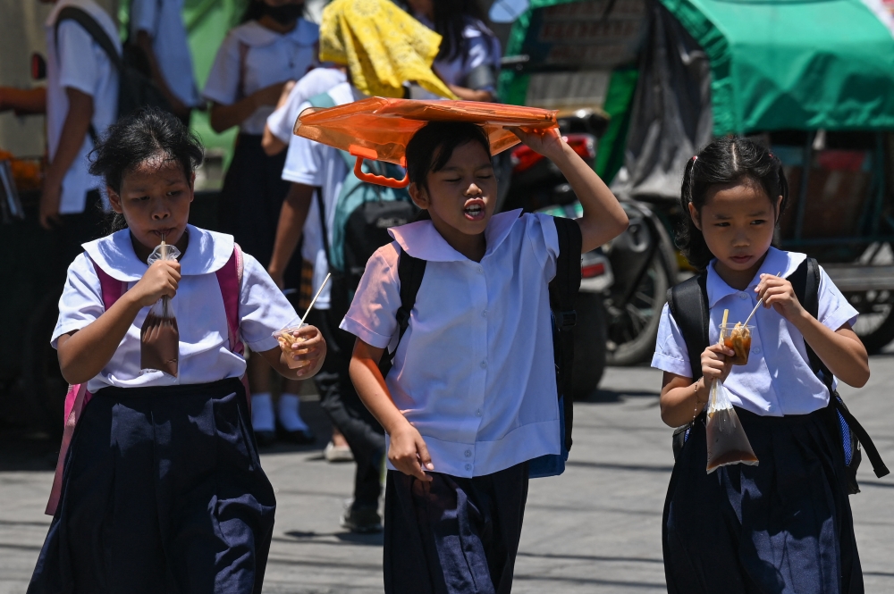 A student uses an envelop to protect herself from the sun during a hot day in Manila on April 2, 2024. — AFP pic