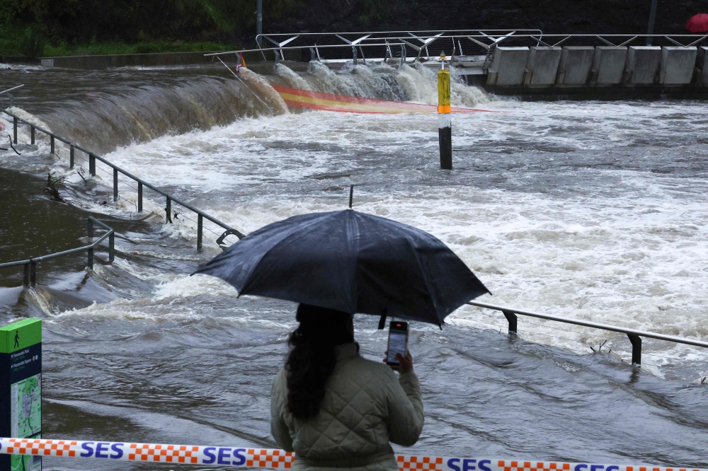 A woman takes pictures of the overflowing Parramatta river at the ferry wharf in Sydney on April 5, 2024, after heavy rain lashed eastern Australia, causing flash flooding and a string of emergency warnings up and down the Pacific coast. ― AFP pic