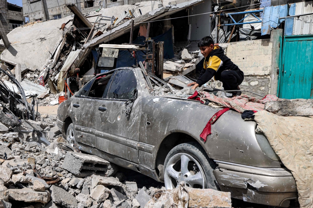 A boy clears rubble from atop a heavily damaged vehicle outside a destroyed building in Rafah in the southern Gaza Strip on April 5, 2024 amid the ongoing conflict in the Palestinian territory between Israel and Hamas. — AFP pic